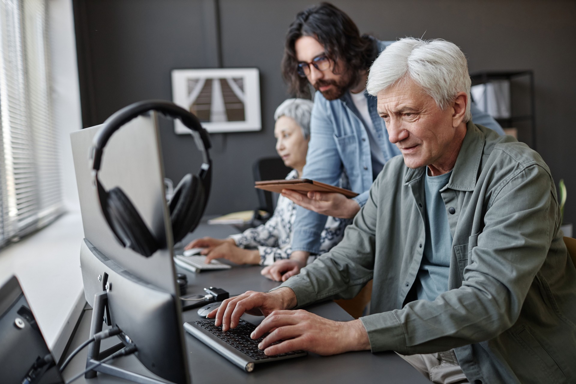 Senior man using computer in class with male instructor helping